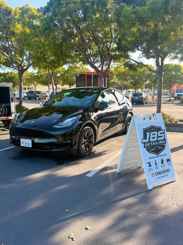 Freshly detailed black sedan beside the JBS Detailing service sign